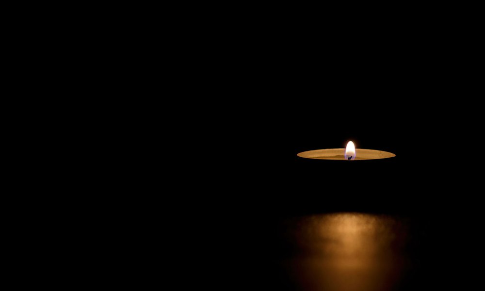 Single lit tin candle in a dark room
